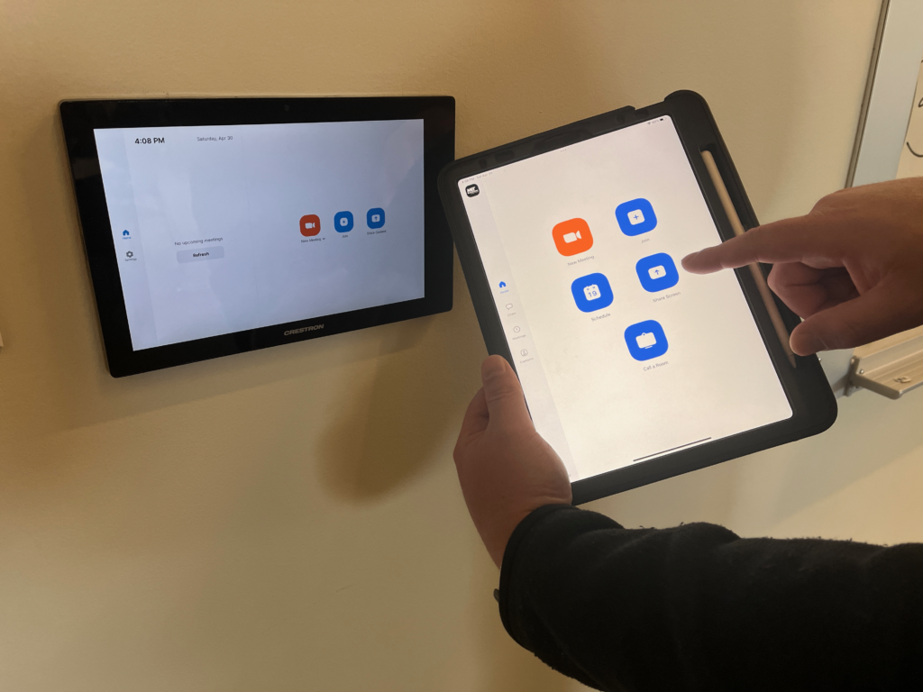 Photo of someone holding an ipad close to a zoom room controller